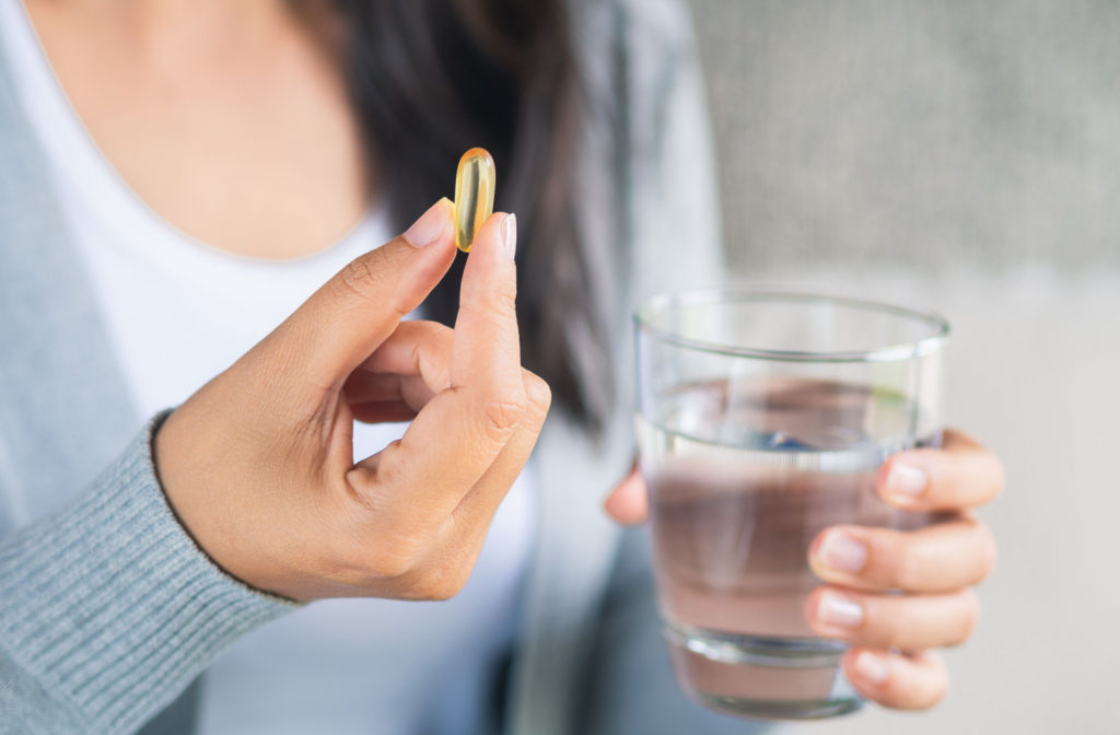 A woman holds a glass of water and an omega-3 capsule, engaging in rehydration and supplement intake.