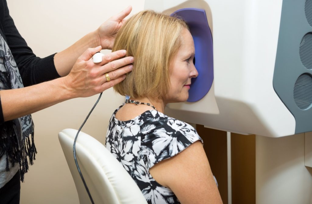 A woman being gently pushed towards a retinal imaging machine by an optometrist.