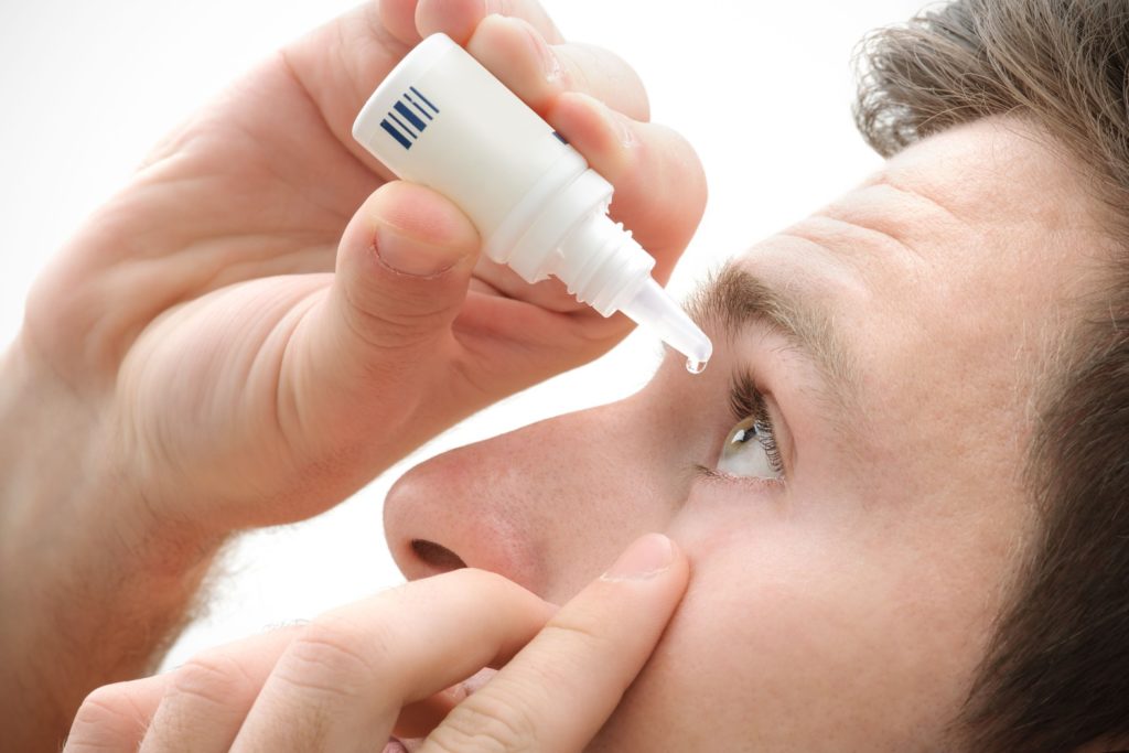 A close-up view of a man carefully applying eye drops to his right eye.