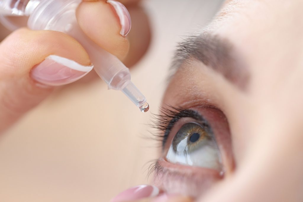 A close-up image of a woman carefully using her right hand to apply eye drops.