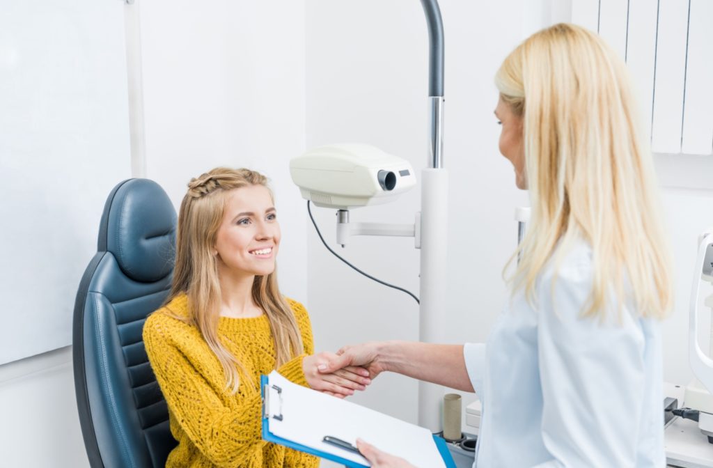 An optometrist shaking hands with a young female patient after discussing the results of her eye exam.