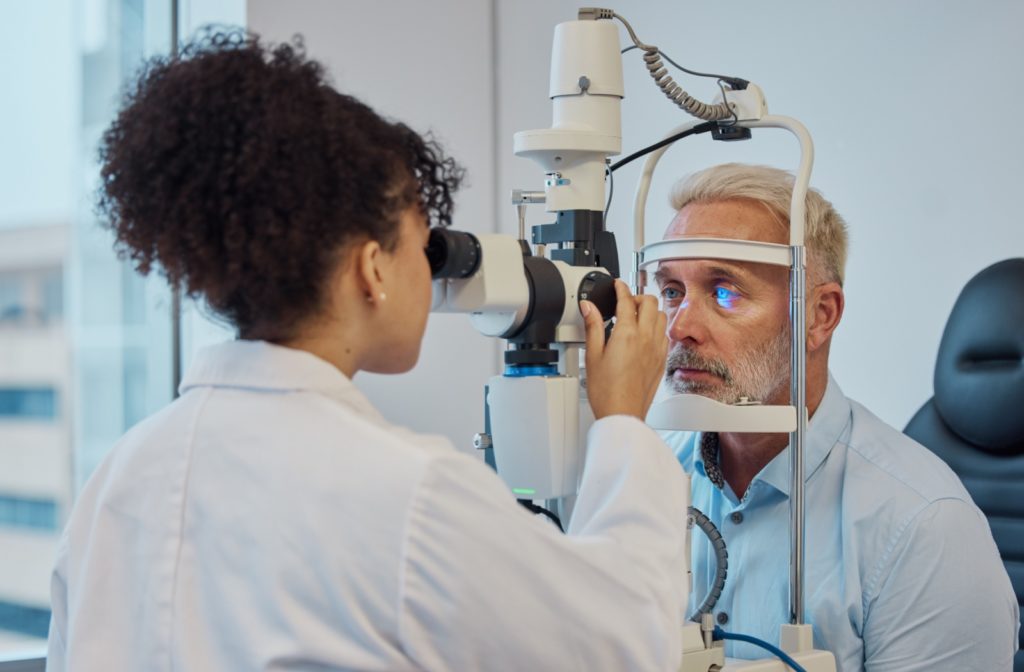 A young optometrist carefully examining a senior man's eyes during an eye exam.