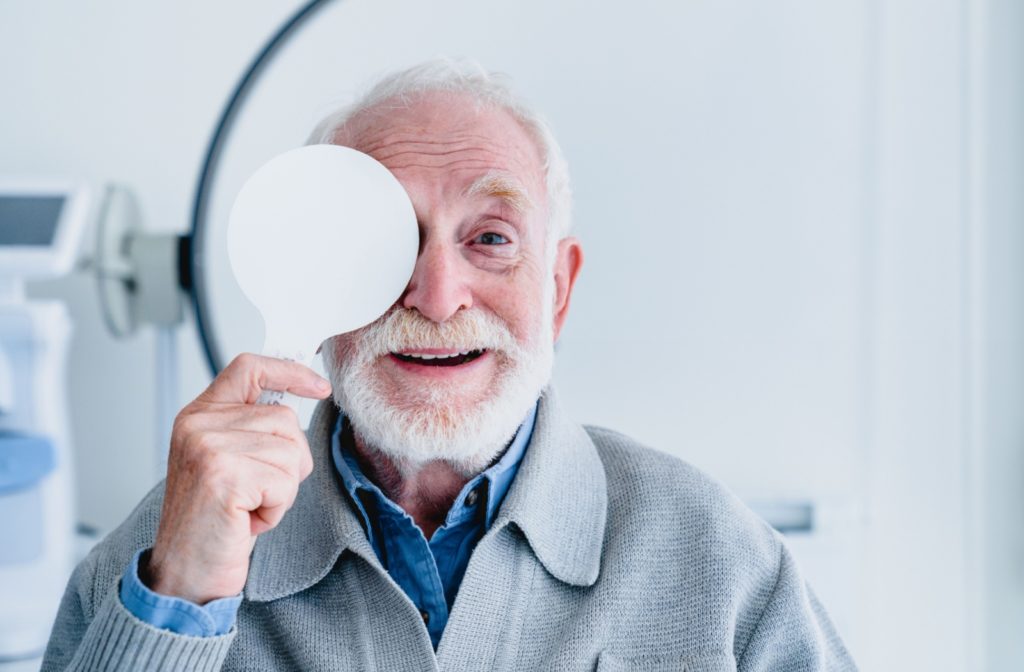 A smiling senior man covering his right eye during a comprehensive eye exam.