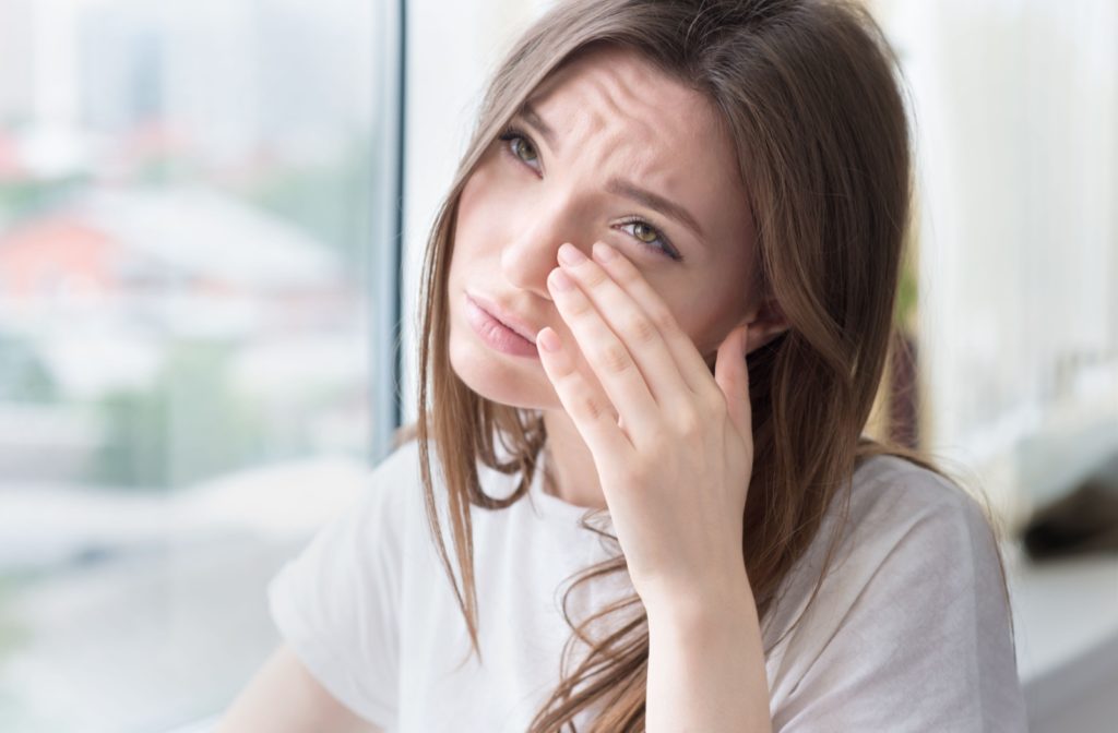 A person standing by a window wipes away their tears while crying.