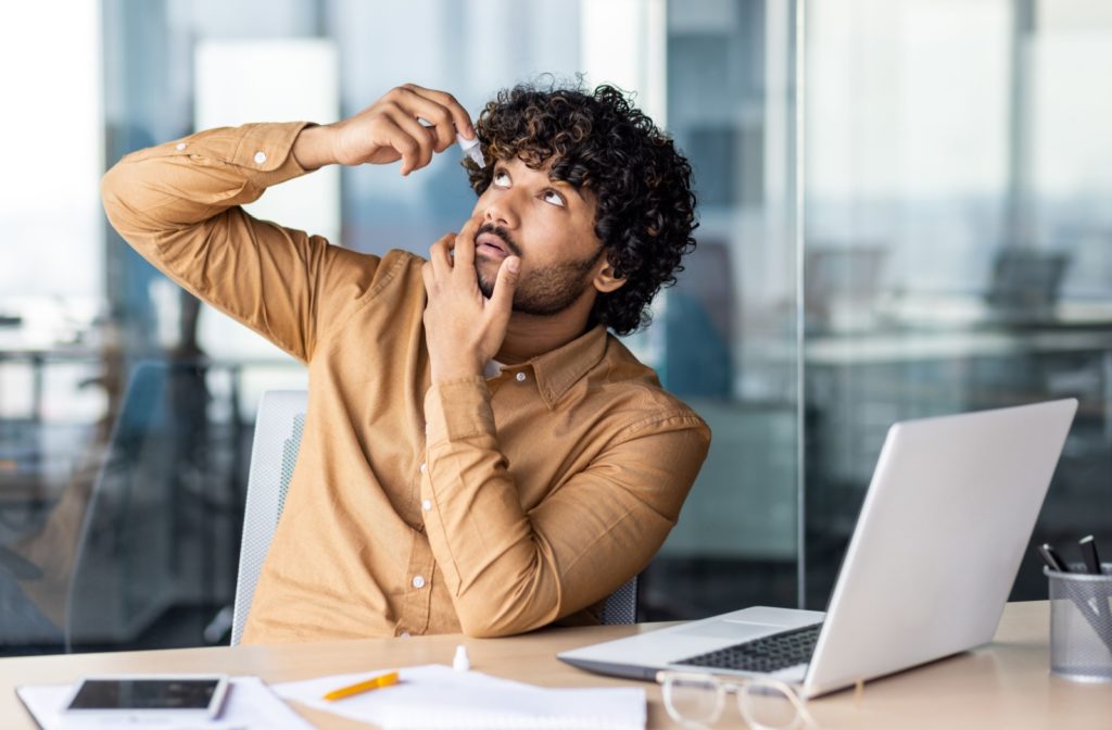 A person suffering from dry eyes at work uses eye drops for relief.