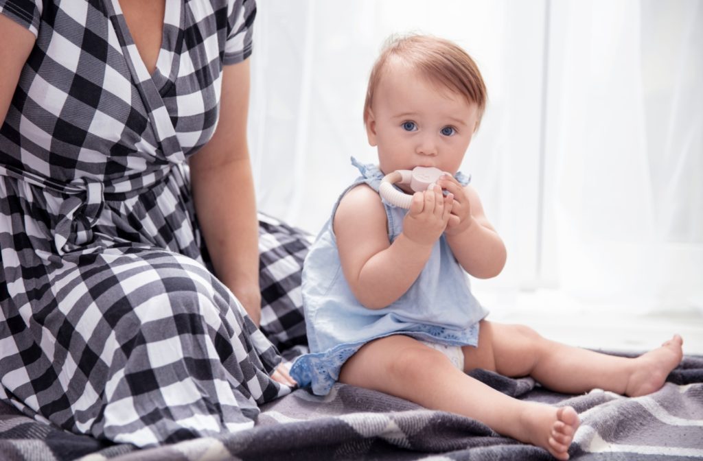 A close-up image of a baby sitting next to a parent with a teether in their mouth.